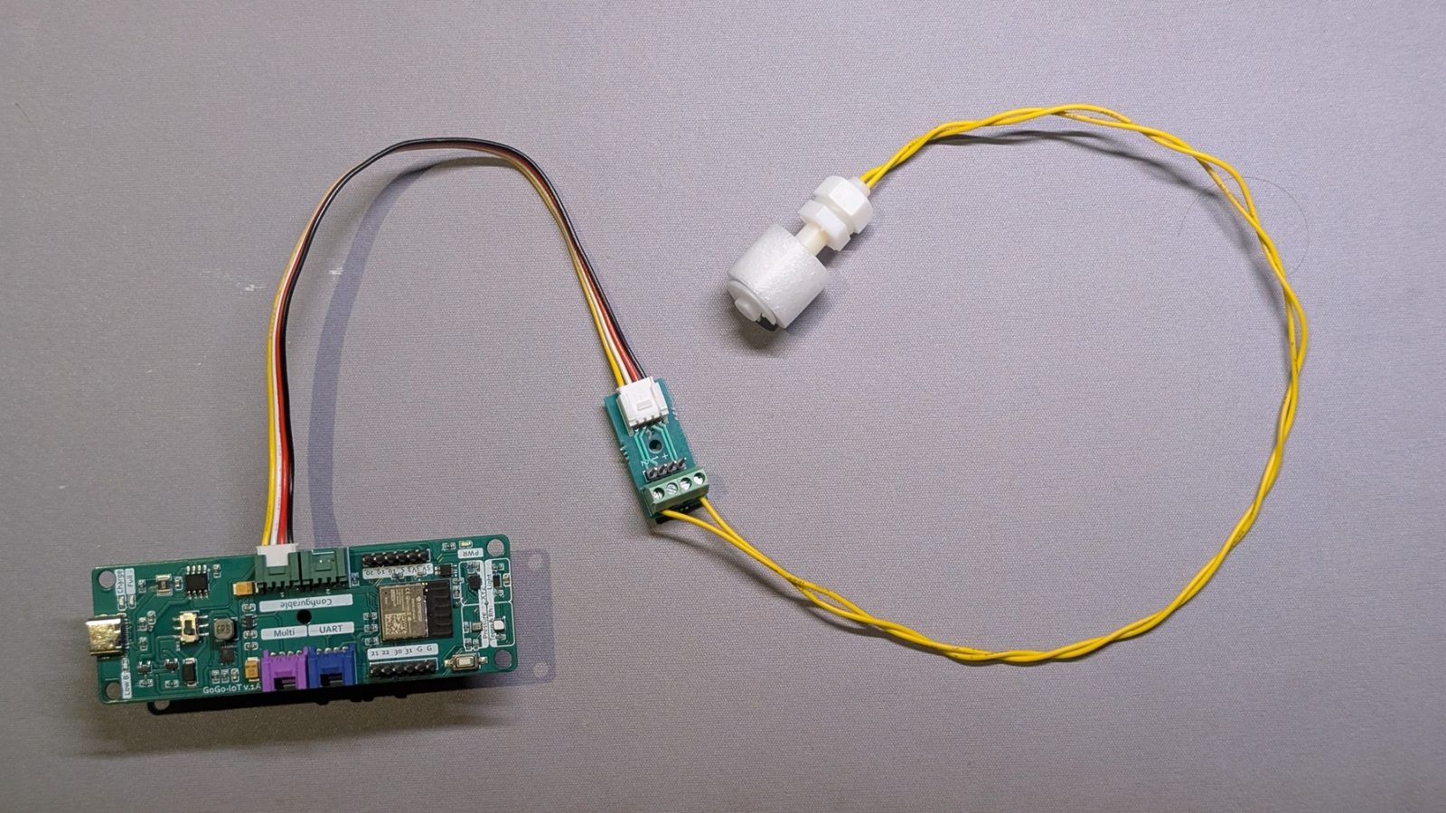 ชุดสวิตช์ลูกลอยที่ต่อกับบอร์ด GoGo-IoT แล้ว: สาย Grove ออกจากบอร์ดไปเข้าตัวแปลงซึ่งเป็นบอร์ดเล็กมีขั้วสกรู และสายสีเหลืองสองเส้นจากตัวแปลงไปยังตัวลูกลอยสีขาว